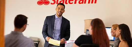 A male speaker, standing in front of a State Farm logo, addresses his fellow workers.